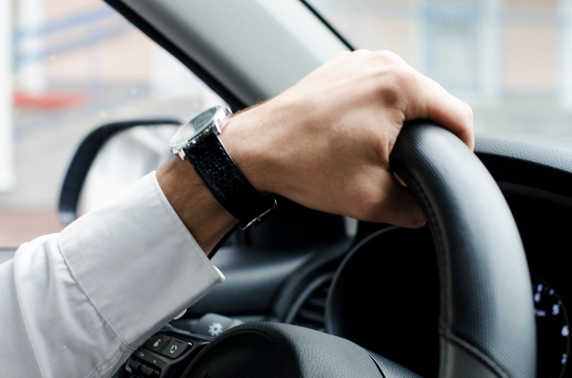 Close-up of a hand with a wristwatch gripping a car steering wheel, showcasing driving focus.