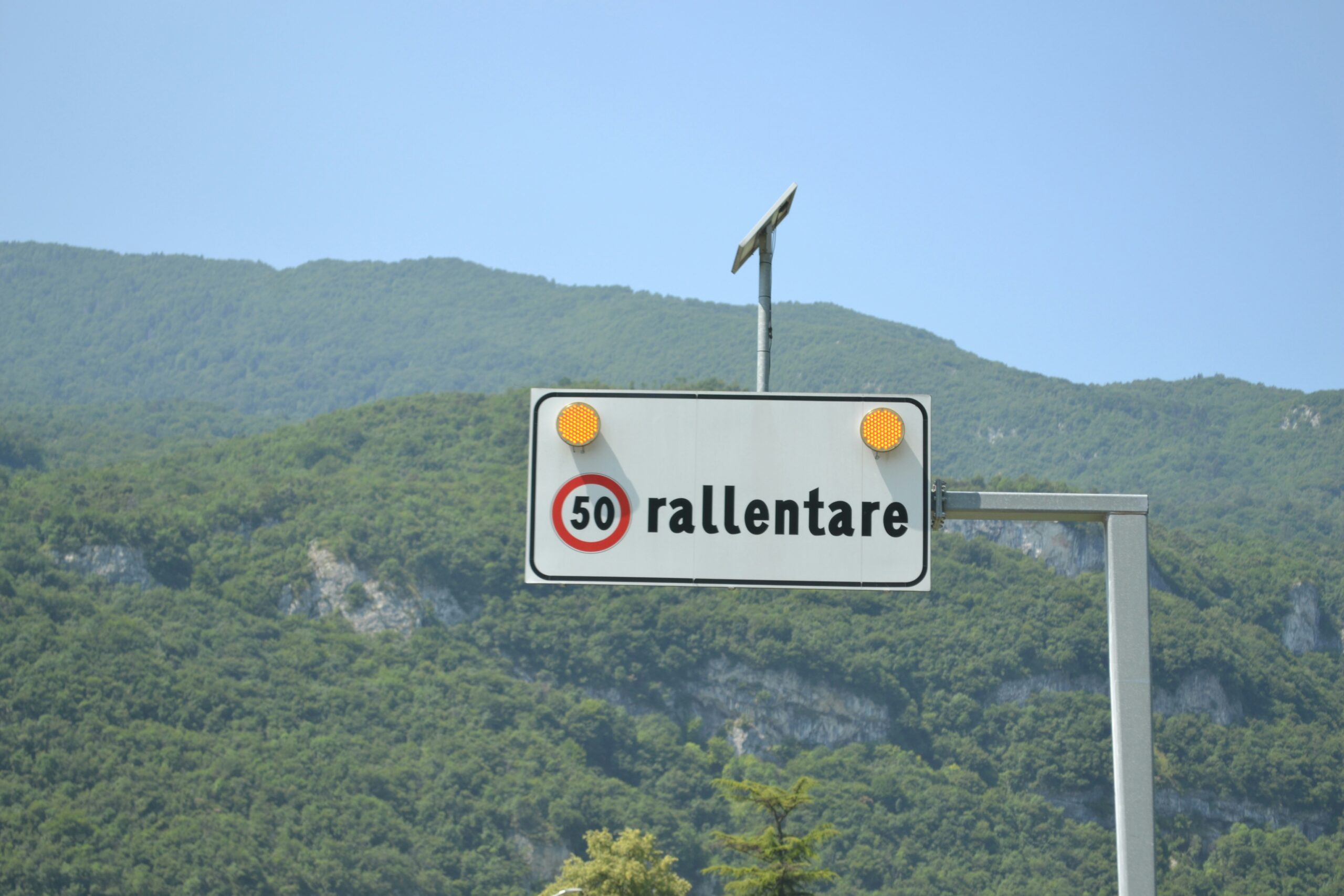 Italian '50 rallentare' road sign with mountain background.