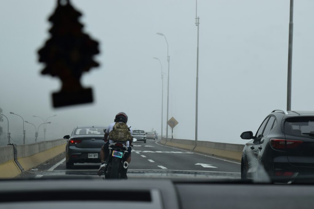 Motorcyclist riding on a foggy highway with cars.