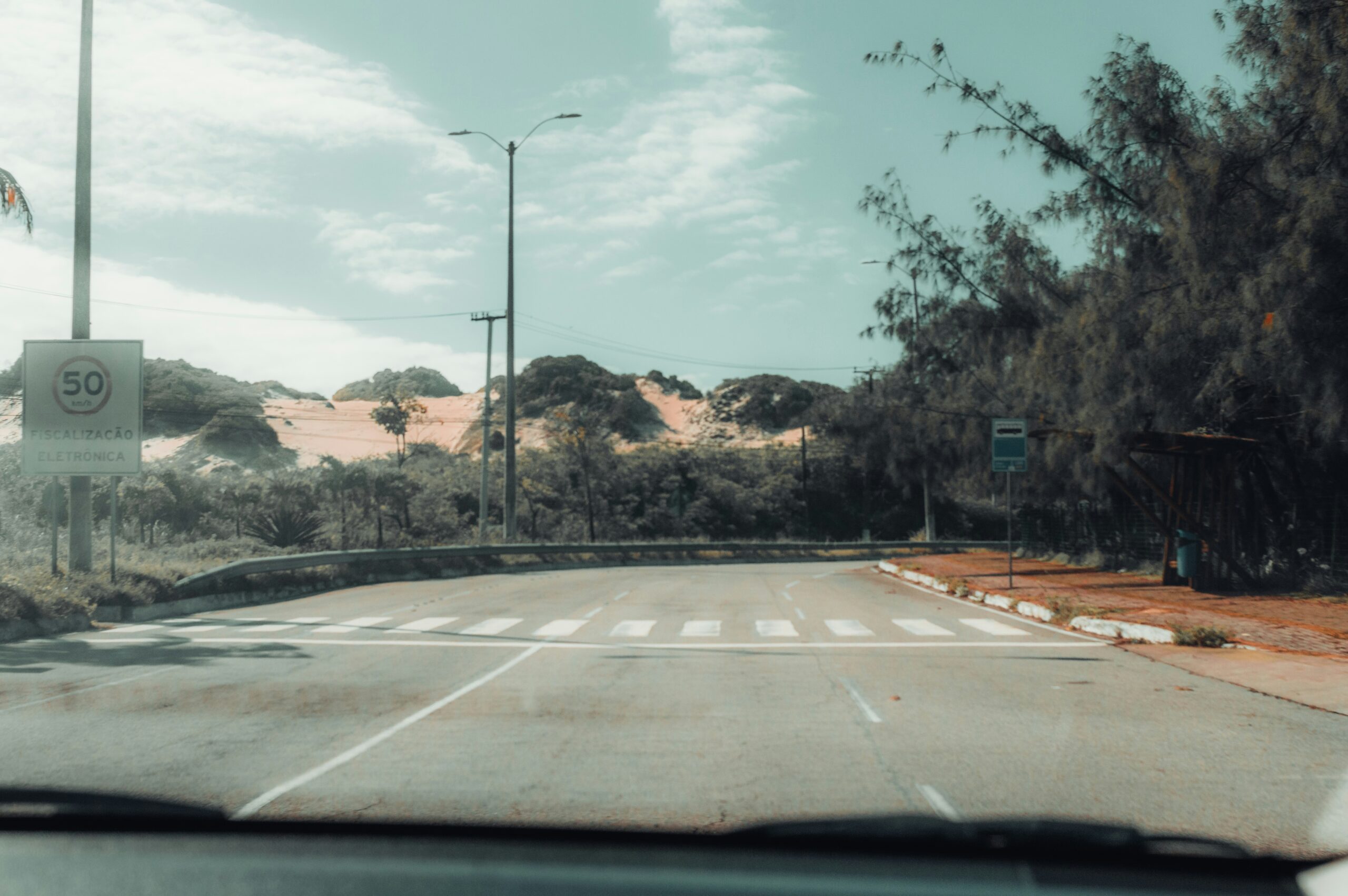 Empty road with crosswalk, sand dunes, and trees.